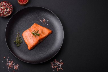 Delicious baked salmon red fish steak with spices and herbs on a dark concrete background
