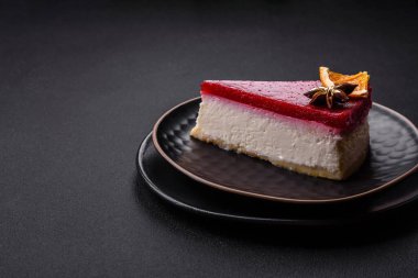 Delicious sweet cheesecake with raspberry jam on a black ceramic plate on a dark concrete background