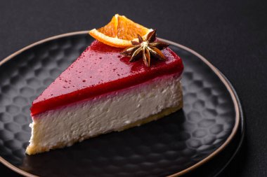 Delicious sweet cheesecake with raspberry jam on a black ceramic plate on a dark concrete background