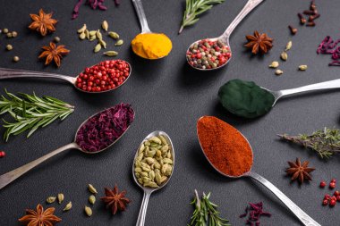 Variation of spices in metal spoons paprika, turmeric, cardamom, a mixture of allspice, thyme, rosemary and salt on a dark concrete background