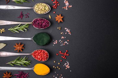 Variation of spices in metal spoons paprika, turmeric, cardamom, a mixture of allspice, thyme, rosemary and salt on a dark concrete background