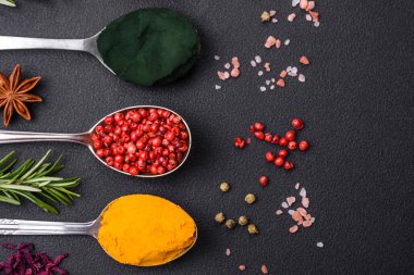 Variation of spices in metal spoons paprika, turmeric, cardamom, a mixture of allspice, thyme, rosemary and salt on a dark concrete background
