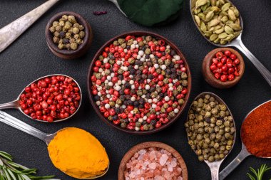Variation of spices in metal spoons paprika, turmeric, cardamom, a mixture of allspice, thyme, rosemary and salt on a dark concrete background
