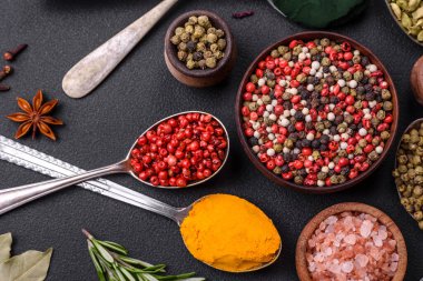 Variation of spices in metal spoons paprika, turmeric, cardamom, a mixture of allspice, thyme, rosemary and salt on a dark concrete background