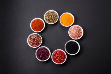 Composition consisting of a variation of several types of spices in white ceramic bowls on a textured concrete background