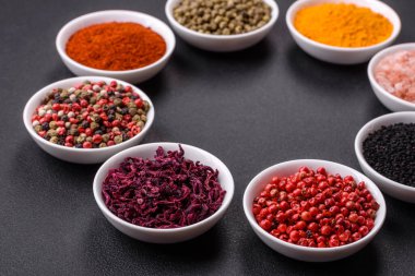Composition consisting of a variation of several types of spices in white ceramic bowls on a textured concrete background