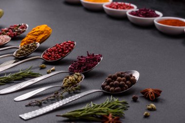 Composition consisting of variations of spices in white bowls and metal spoons on a dark concrete background