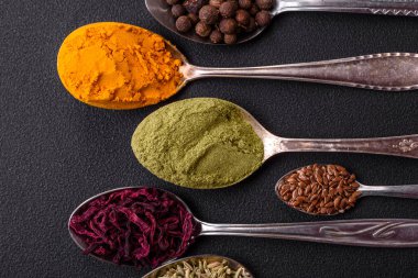 Composition consisting of variations of spices in white bowls and metal spoons on a dark concrete background