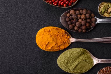 Composition consisting of variations of spices in white bowls and metal spoons on a dark concrete background