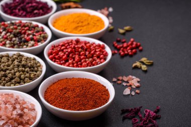 Composition consisting of variations of spices in white bowls and metal spoons on a dark concrete background