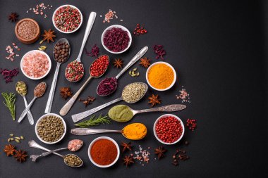 Composition consisting of variations of spices in white bowls and metal spoons on a dark concrete background