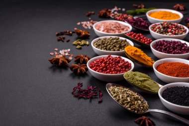 Composition consisting of variations of spices in white bowls and metal spoons on a dark concrete background