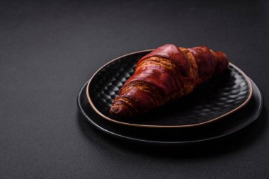 Delicious crispy croissant with chocolate on a black ceramic plate on a dark concrete background