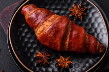Delicious crispy croissant with chocolate on a black ceramic plate on a dark concrete background