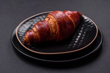 Delicious crispy croissant with chocolate on a black ceramic plate on a dark concrete background