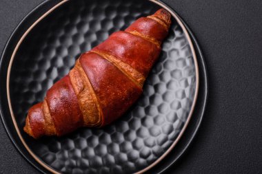 Delicious crispy croissant with chocolate on a black ceramic plate on a dark concrete background