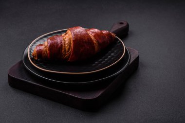 Delicious crispy croissant with chocolate on a black ceramic plate on a dark concrete background