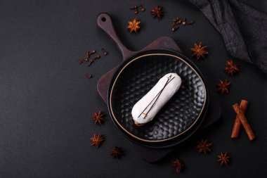 Delicious fresh profiterole or eclair with chocolate on a black ceramic plate on a dark concrete background