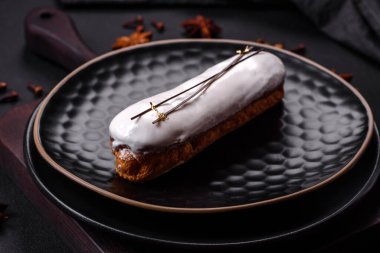 Delicious fresh profiterole or eclair with chocolate on a black ceramic plate on a dark concrete background