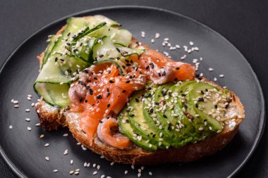 Fresh tasty sandwich with salmon, avocado and sesame and flax seeds on a dark concrete background