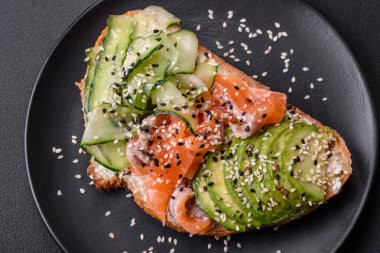 Fresh tasty sandwich with salmon, avocado and sesame and flax seeds on a dark concrete background