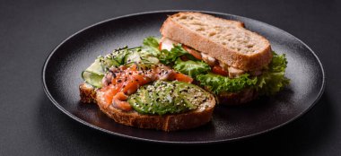 Fresh tasty sandwich with salmon, avocado and sesame and flax seeds on a dark concrete background