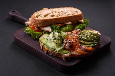 Fresh tasty sandwich with salmon, avocado and sesame and flax seeds on a dark concrete background