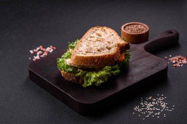 Fresh tasty sandwich with chicken, tomatoes and lettuce on a black plate on a dark concrete background