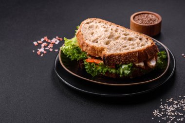 Fresh tasty sandwich with chicken, tomatoes and lettuce on a black plate on a dark concrete background