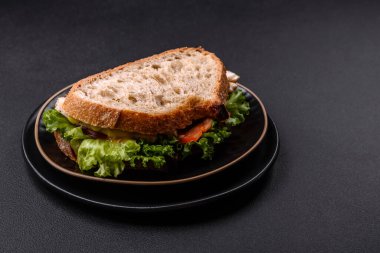 Fresh tasty sandwich with chicken, tomatoes and lettuce on a black plate on a dark concrete background