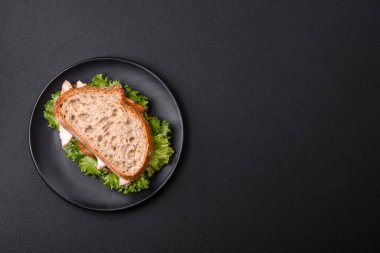 Fresh tasty sandwich with chicken, tomatoes and lettuce on a black plate on a dark concrete background