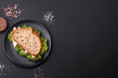 Fresh tasty sandwich with chicken, tomatoes and lettuce on a black plate on a dark concrete background