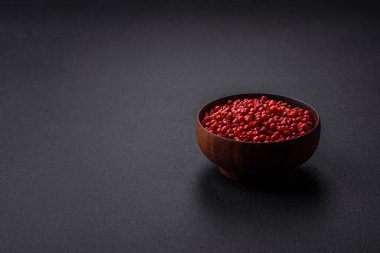 Spice, allspice peas in red or pink color in a wooden bowl on a black concrete background. Asian cuisine