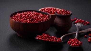 Spice, allspice peas in red or pink color in a wooden bowl on a black concrete background. Asian cuisine