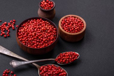 Spice, allspice peas in red or pink color in a wooden bowl on a black concrete background. Asian cuisine
