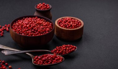 Spice, allspice peas in red or pink color in a wooden bowl on a black concrete background. Asian cuisine