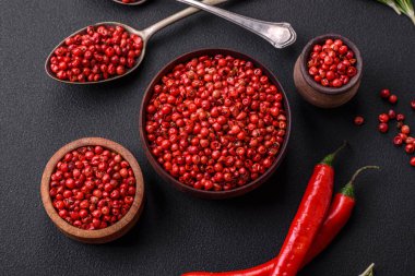 Spice, allspice peas in red or pink color in a wooden bowl on a black concrete background. Asian cuisine