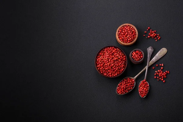 Spice, allspice peas in red or pink color in a wooden bowl on a black concrete background. Asian cuisine