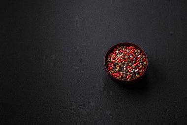 Spice allspice of different colors pink, white, green not ground in a wooden saucer on a dark concrete background