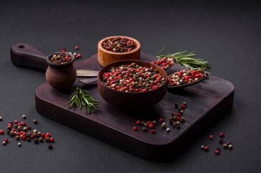 Spice allspice of different colors pink, white, green not ground in a wooden saucer on a dark concrete background