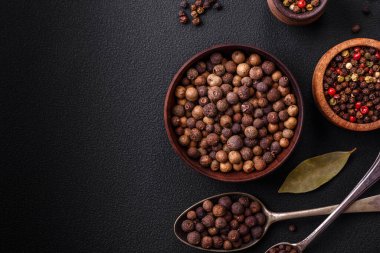 Spice allspice brown color not ground in a wooden saucer on a dark concrete background