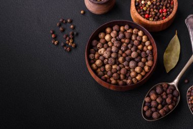 Spice allspice brown color not ground in a wooden saucer on a dark concrete background