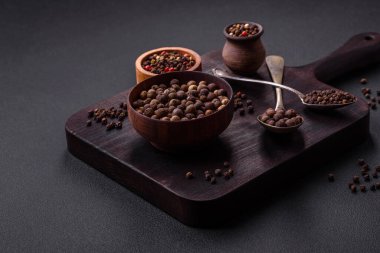 Spice allspice brown color not ground in a wooden saucer on a dark concrete background
