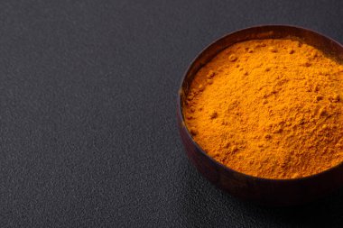 Bright yellow turmeric or curry spice for Asian food preparation on dark concrete background