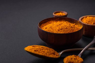 Bright yellow turmeric or curry spice for Asian food preparation on dark concrete background