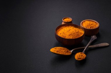 Bright yellow turmeric or curry spice for Asian food preparation on dark concrete background