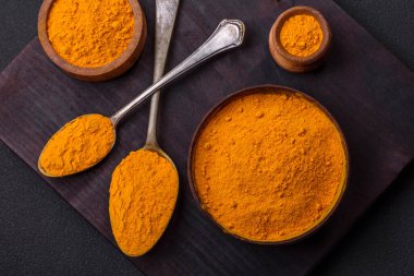 Bright yellow turmeric or curry spice for Asian food preparation on dark concrete background
