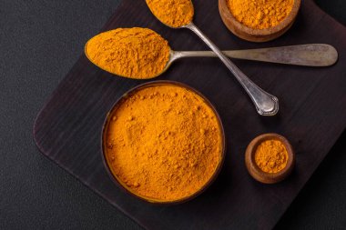 Bright yellow turmeric or curry spice for Asian food preparation on dark concrete background