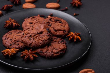 Delicious chocolate cookies with nuts on a black ceramic plate on a dark concrete background