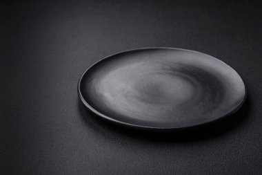 Empty ceramic round plate on dark textured concrete background. Cutlery, preparation for dinner